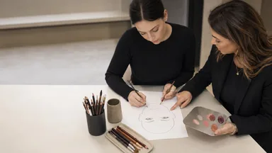 Allieva e docente adulte progettano una face chart make-up originale usando matite, pennelli dedicati e una palette pulita