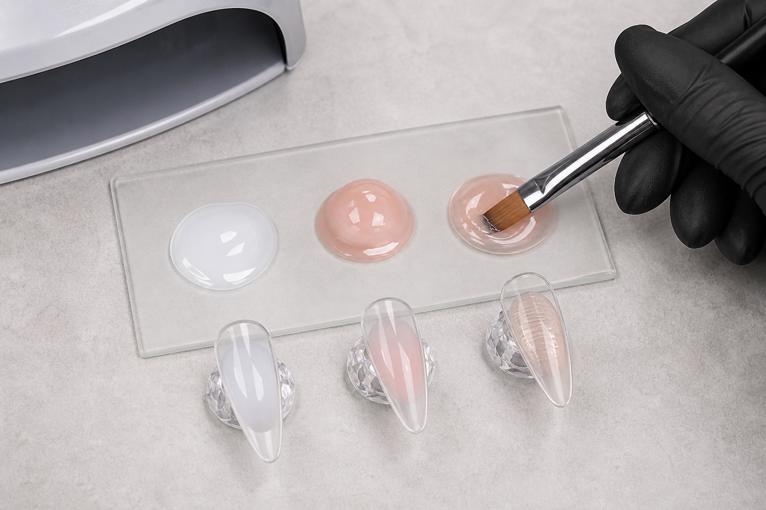 Confronto professionale di tre consistenze di gel costruttore su palette e tip trasparenti con pennello e lampada UV LED