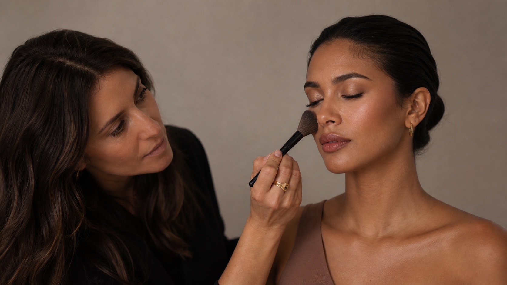 Make-up artist adulta applica blush e bronzer con un pennello professionale sul viso di una modella adulta in luce neutra