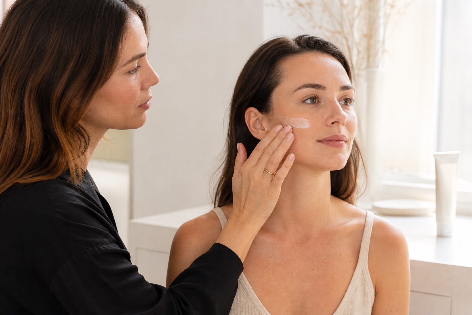 Make-up artist applica una quantità uniforme di crema solare sul viso di una cliente adulta prima del trucco