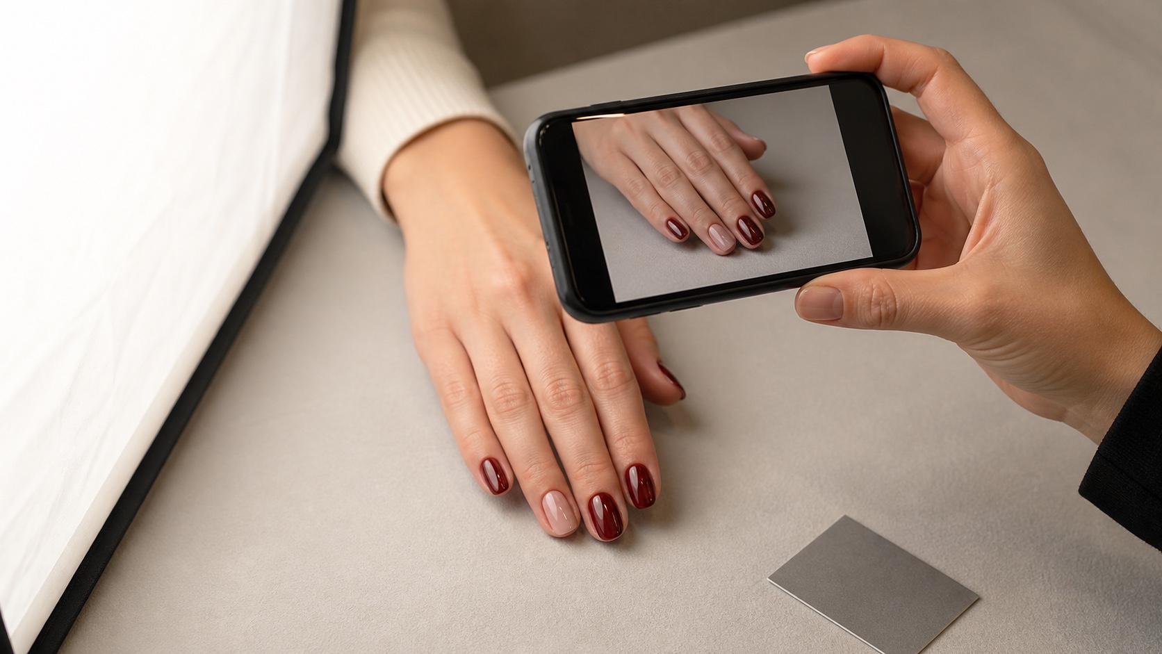 Onicotecnica fotografa una manicure burgundy e nude con smartphone, luce diffusa e riferimento neutro