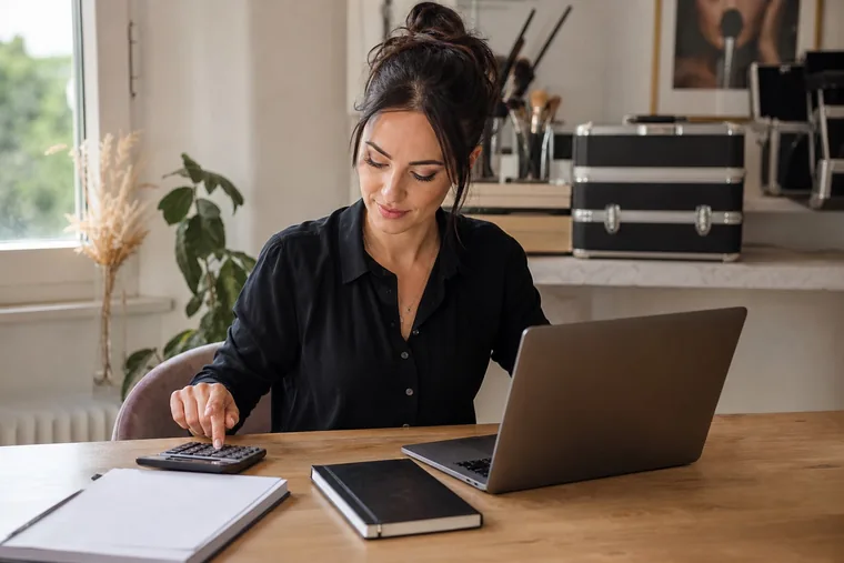Make-up artist controlla i conti con calcolatrice e laptop alla propria scrivania