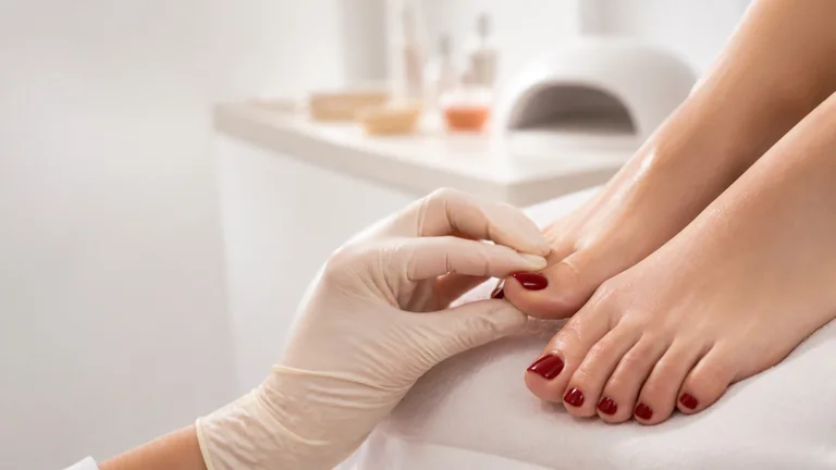 Operatrice con guanti osserva l’alluce con semipermanente rosso; i piedi sono appoggiati su un telo