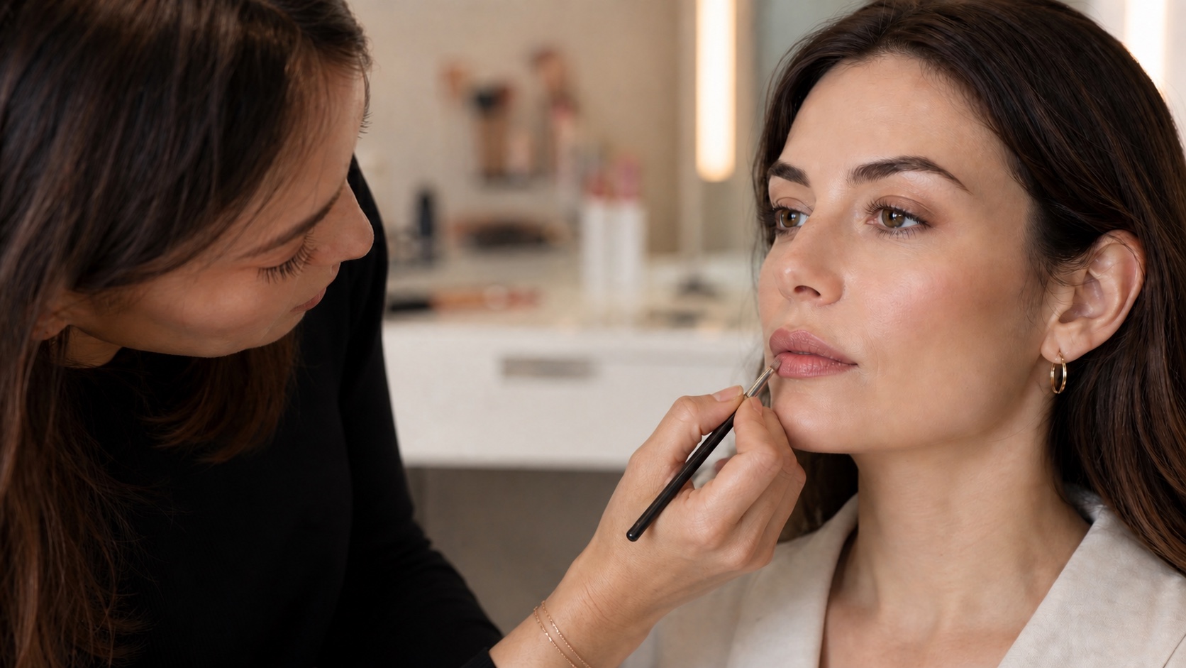 Make-up artist adulta definisce il contorno labbra di una modella adulta con un pennello fine in uno studio professionale