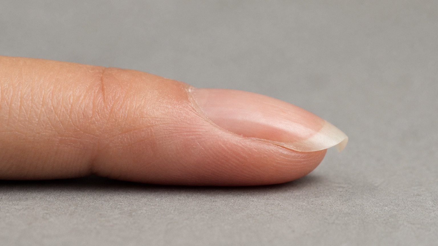 Side profile of an intact natural nail whose free edge curves downward below the finger axis