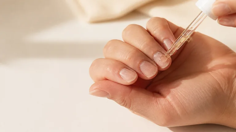 Contagocce con olio vicino a unghie naturali corte dalla superficie irregolare
