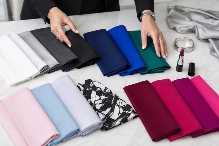 Neutral, blue, green, pale and berry-colored fabrics beside a black-and-white print, silver jewelry and plum lipstick.